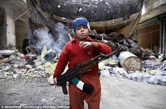 المحارب الصغير: أحمد، ذو السنين السبع، و ابن أحد مقاتلي الجيش السوري الحر، يقف أمام متراس / حاجز مساعداً رفاقه من الجيش السوري الحر في حي صلاح الدين.